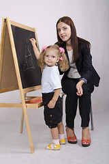 Image showing Little girl draws on Board house, educator helps her