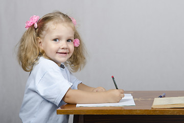 Image showing Little girl sitting at table and wrote in notebook