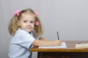 Image showing Little girl sitting at table and wrote in notebook