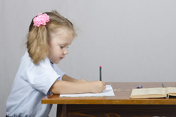 Image showing Little girl sitting at table and wrote in notebook