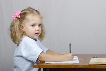 Image showing Little girl sitting at table and wrote in notebook