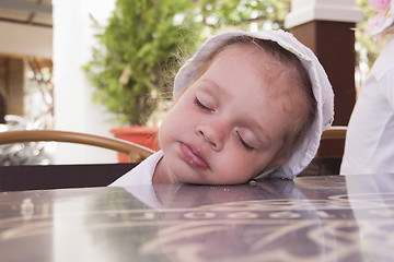 Image showing Two-year-old girl asleep at a table in street cafe