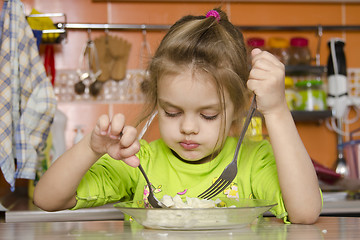 Image showing girl eats with a fork and spoon sitting at table in kitchen