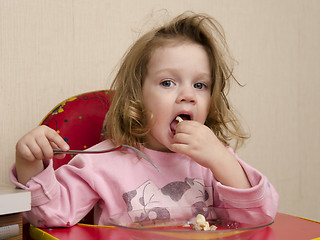 Image showing Two-year-old girl eats with a fork at table in kitchen