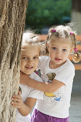 Image showing Two children peep out from behind a tree