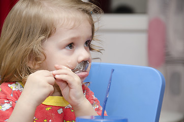 Image showing girl is licking spoon, eats cake, and looks right