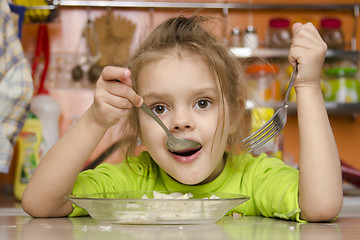 Image showing girl eats with a fork and spoon sitting at table in kitchen