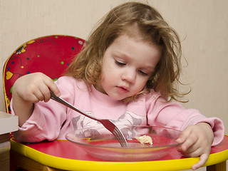 Image showing Two-year-old girl eats with a fork at table in kitchen