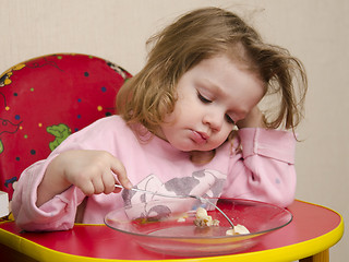 Image showing Two-year-old girl eats with a fork at table in kitchen