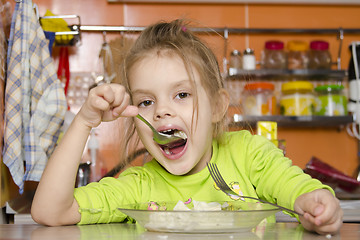 Image showing girl eats with a fork and spoon sitting at table in kitchen