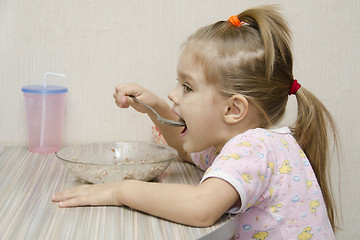 Image showing Girl eating porridge sitting at table