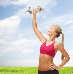 Image showing smiling woman lifting steel dumbbell