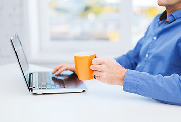 Image showing male hand with cup of tea or coffee and laptop