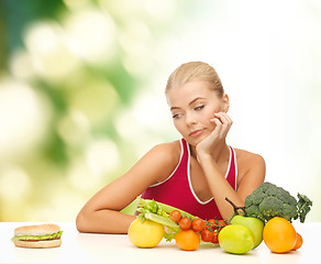 Image showing doubting woman with fruits and hamburger