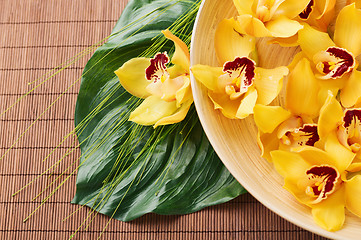 Image showing orchid flowers in bowl with green leaf on mat