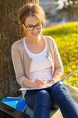 Image showing smiling teenager in eyeglasses writing in notebook