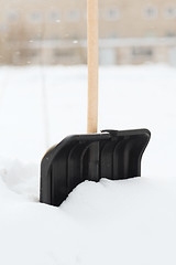 Image showing black snowshowel with wooden handle in snow pile