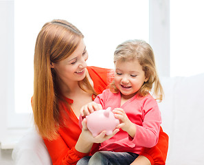 Image showing happy mother and daughter with small piggy bank