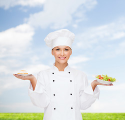 Image showing smiling female chef with salad and cake on plates