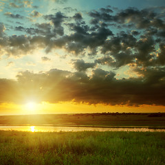 Image showing orange sunset with dark clouds over river