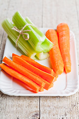 Image showing bundle of fresh green celery stems and carrot in plate