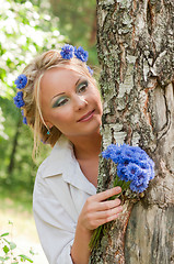 Image showing Woman with blue flowers peeking from behind a tree