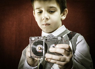 Image showing Rolled cassette strip with a pencil. Boy hold cassette tape.