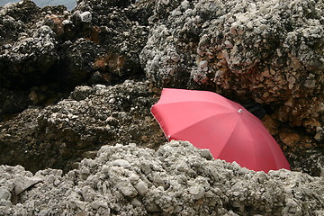 Image showing Red parasol hidden among rocks