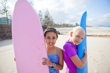 Image showing Two happy young girls holding surfboards at beach