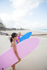 Image showing Two cute young girls walking together with surfboards at beach