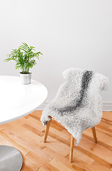 Image showing Chair covered with sheepskin, and plant on a white table