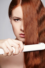 Image showing Redheaded woman with hair straightening irons