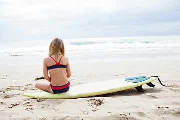 Image showing Young girl sitting on surfboard on beach