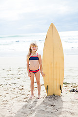 Image showing Young girl standing with surfboard on beach