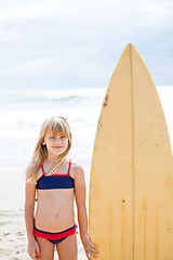 Image showing Smiling young girl standing next to surfboard