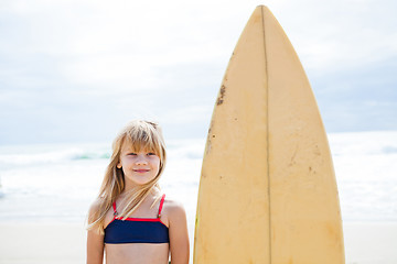 Image showing Smiling young girl standing next to surfboard
