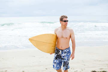 Image showing Serious looking man walking with surfboard at beach