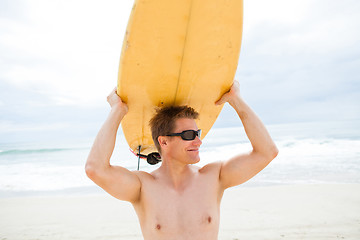 Image showing Smiling man resting surfboard on head at beach