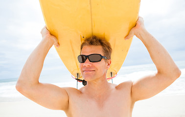 Image showing Smiling man resting surfboard on head at beach