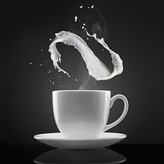 Image showing white cup with hot liquid and milk splash on black