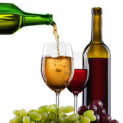 Image showing White wine pouring into glass with grape and bottles isolated