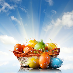 Image showing color easter eggs in basket against blue sky and clouds