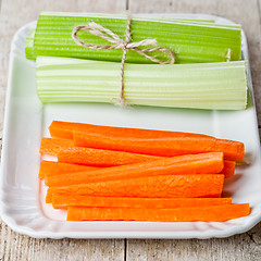 Image showing bundle of fresh green celery stems and carrot in plate