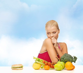 Image showing doubting woman with fruits and hamburger