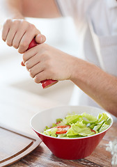 Image showing close up of male hands flavouring salad in a bowl