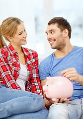 Image showing smiling couple with piggybank sitting on sofa