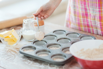 Image showing close up of hand filling muffins molds with dough