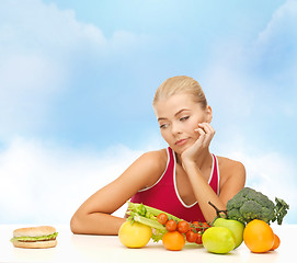 Image showing doubting woman with fruits and hamburger