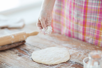 Image showing closeup of female hand sprinkling dough with flour