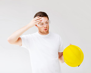 Image showing male builder in safety glasses taking off helmet